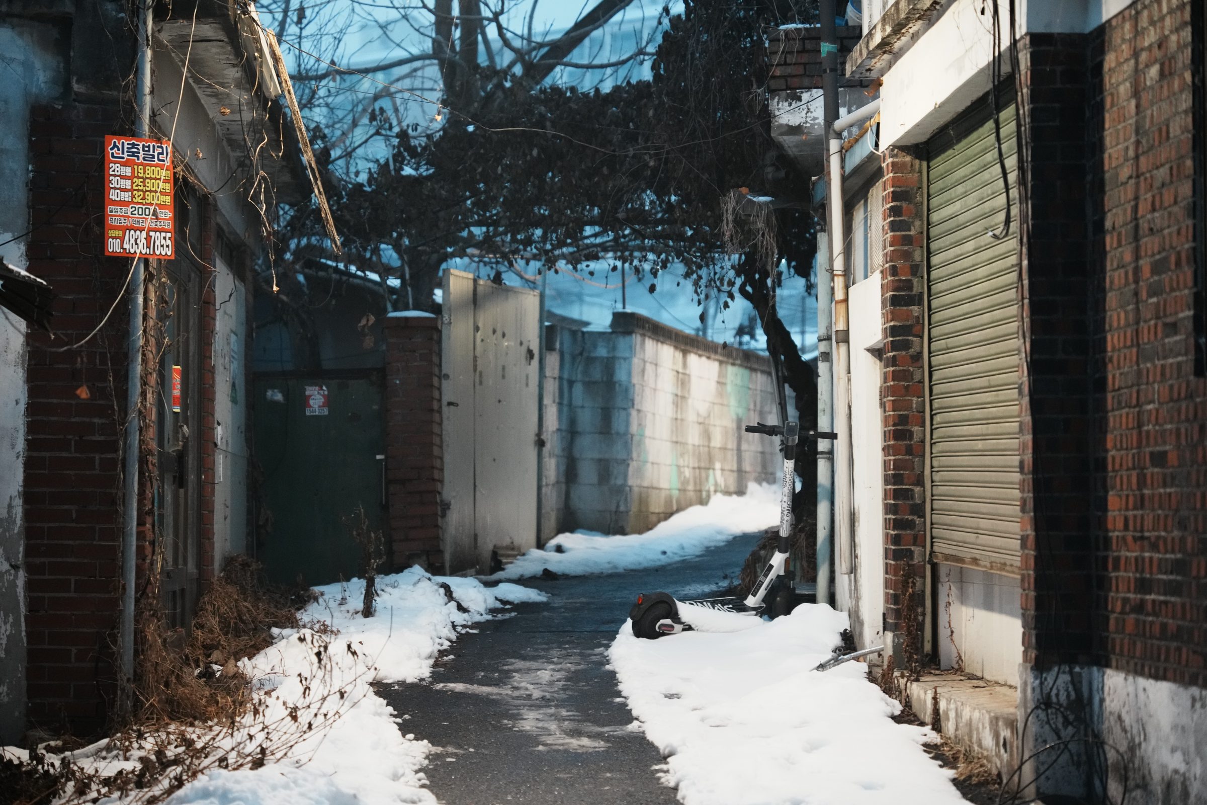 눈 내린 골목과 세워진 전동킥보드, 신축빌라 안내판