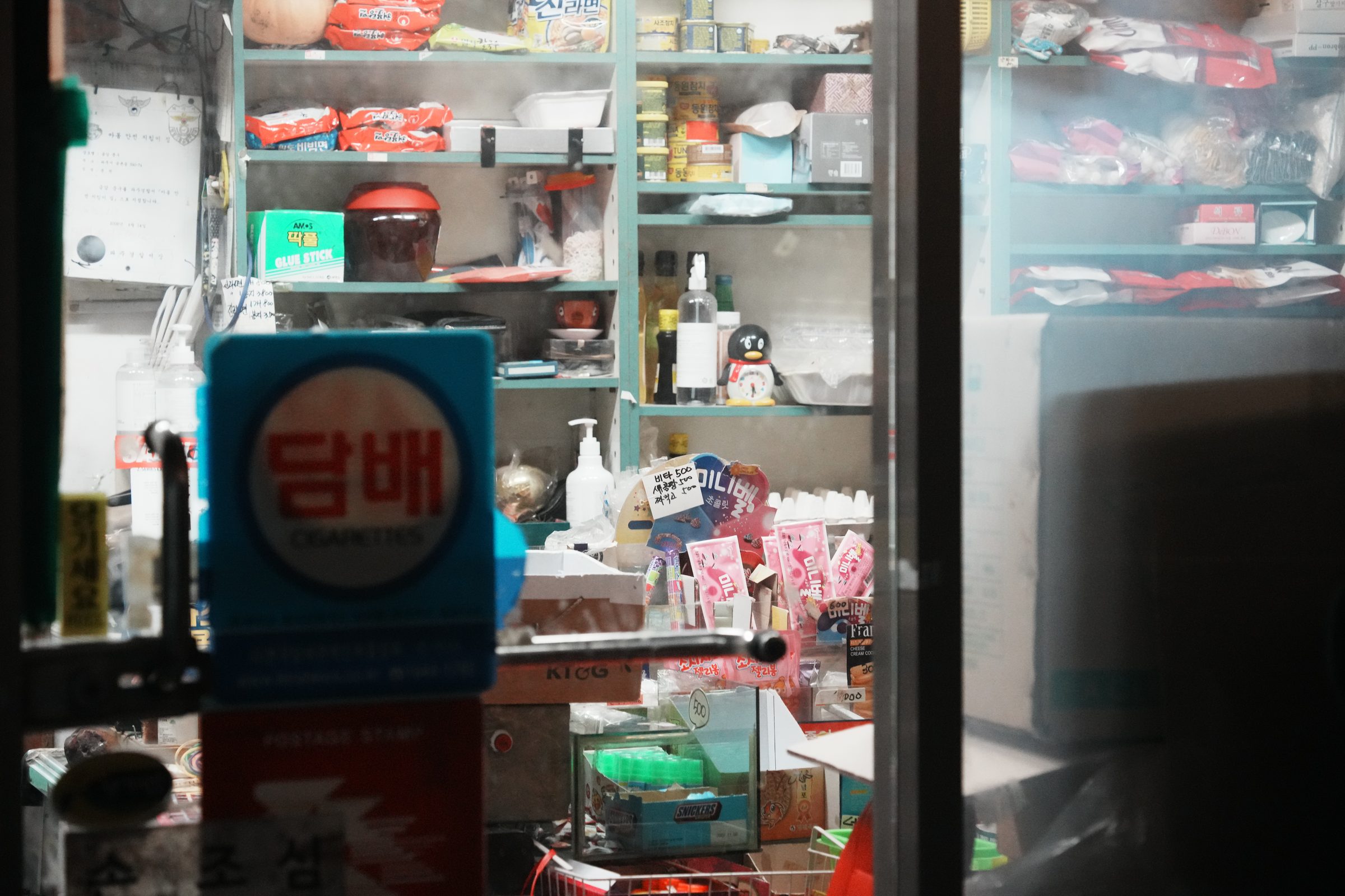 유리 너머로 본 오래된 구멍가게 내부와 담배 간판